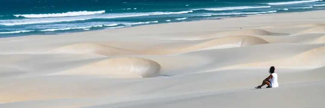 Ein einzelner Spaziergänger geht entlang des weiten, goldgelben Strandes im Naturreservat Morro de Areia auf Boa Vista.