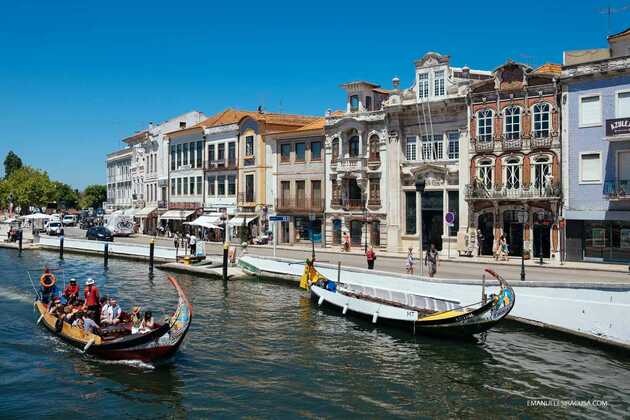 Bunte Häuserfassade in Aveiro, dem Venedig im Norden Portugals, mit Flusslauf davor und Boots-Ausflüglern.