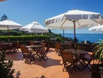Caloura Hotel Resort – Sonnige Terrasse mit Meerblick und gemütlichen Sitzgelegenheiten für entspannte Urlaubsmomente auf São Miguel.