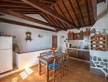 Casas do Capelo auf Faial, gemütliche rustikale Küche mit holzgetäfelter Decke, Esstisch mit Stühlen und Wandregal mit Geschirr.