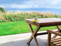 Holztisch mit Tasse auf der Terrasse der Areias da Prainha mit Blick auf Wiese und Atlantik vor dramatischer Wolkenkulisse