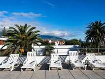 Antillia Hotel Apartments auf Sao Miguel, sonnige Dachterrasse mit Liegestühlen und herrlichem Blick auf Palmen und Berge – perfekt zum Entspannen.