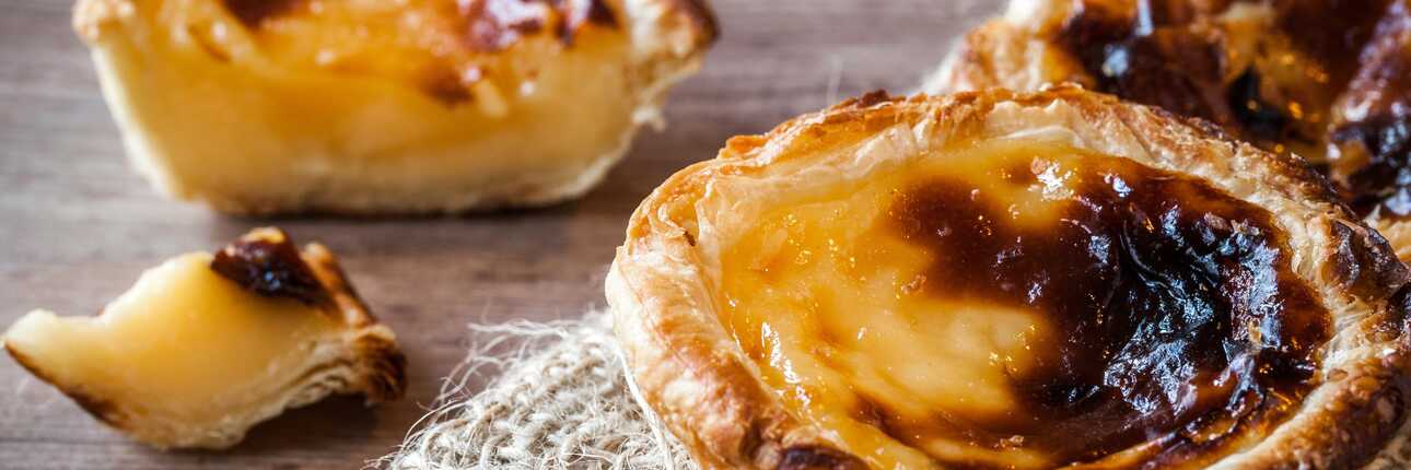 Nahaufnahme eines frisch gebackenen Pastel de Nata mit karamellisierter Oberfläche auf rustikalem Untergrund.