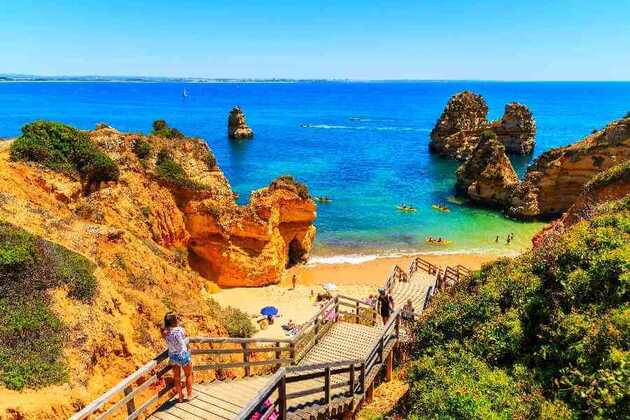 Holztreppe führt hinunter zu einem Traumstrand, eingebettet von Felsen und dem türkisblauen Meer - an der Algarve Küste in Portugal.
