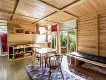 Azul Singular auf der Insel Faial – Helles, gemütliches Zimmer mit Holzwänden, einer kleinen Küche, einem Esstisch, Stühlen und einer Sitzbank neben einem großen Fenster mit Blick auf einen grünen Garten.