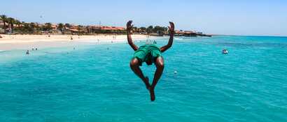 Ein junger Mann springt bei strahlendem Sonnenschein vom Steg ins türkisfarbene Meer auf den Kapverden.