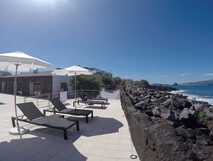 Sonnenterrasse der Baía da Barca Apartments mit Pool, Liegen und Ausblick auf das Meer und die Felsküste von Pico