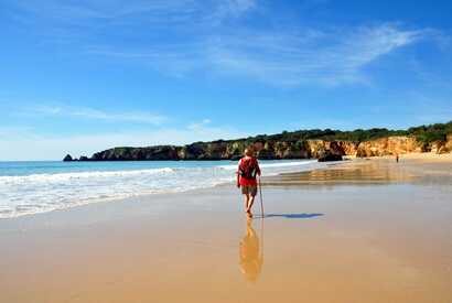 Mann wandert mit Wanderstab am Strand entlang