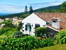 Casas do Capelo: Traditionelles weißes Ferienhaus mit Vulkansteinmauer, grünen Fensterläden und Blick auf die grüne Hügellandschaft der Azoren