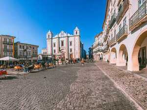 Der Hauptplatz der Stadt Evora, Portugal, umgeben von einer schicken Häuserreihe und vielen Freisitzen direkt unter blauem Himmel.