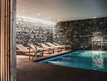 Sensi Azores Nature & Spa auf Sao Miguel – Entspannen im stilvollen Indoor-Pool mit Wasserfall und bequemen Liegen inmitten natürlicher Steinwände.