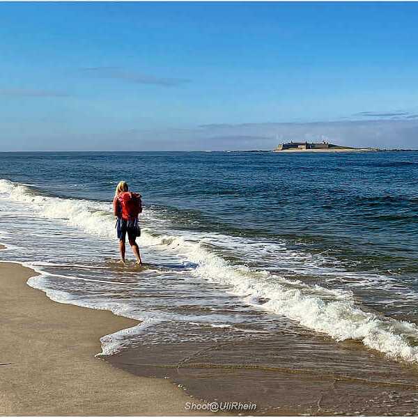 Ein Wanderer geht barfuß am Atlantikstrand entlang, die Wellen rollen ans Ufer in Nordportugal.