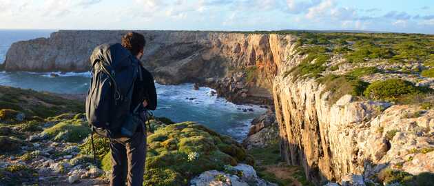 Wanderin mit Blick auf die Bucht, welche an der Westküste Portugals von hohen Klippen umrahmt wird.