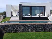 Moderne Villa Casa das Cinco auf den Azoren mit Pool, großer Fensterfront und stilvoller Terrasse mit weißen Loungestühlen