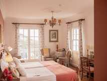 Freundlich eingerichtetes Doppelzimmer mit rosa Details, Sessel-Ecke und natürlichem Licht