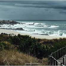 Holzsteg führt durch Dünenlandschaft zu einem wilden Atlantikstrand mit hohen Wellen in Nordportugal.