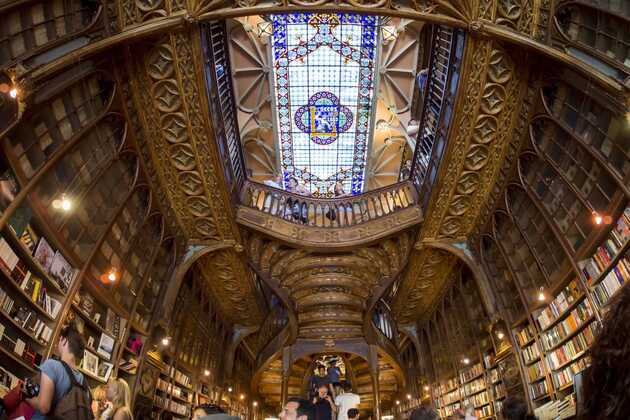 Blick nach oben zur Decke der Livraria Lello, die das Licht durch bunte Glasfliesen scheinen lässt.