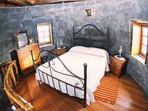 Gemütliches Schlafzimmer in einer restaurierten Windmühle mit Natursteinwänden, Holzboden und romantischem Metallbett