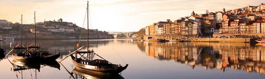 Porto – die kleine Schwester von Lissabon – im Sonnenuntergang mit Blick auf den Hafen und zwei Booten im Vordergrund.
