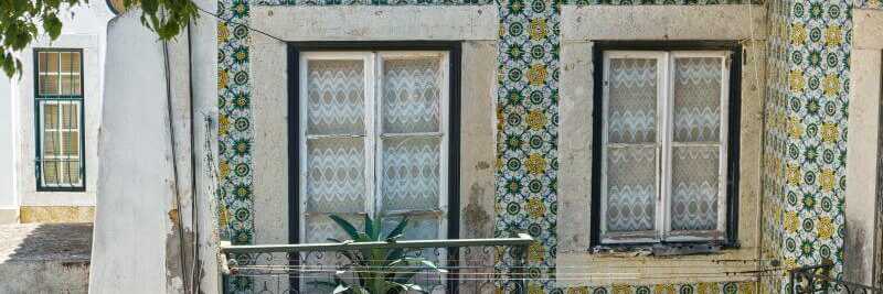 Eine Hauswand mit Balkon, komplett verziert mit grün-gelben Azulejos.