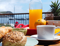 Casa da Baia auf Faial, Frühstück mit frischem Brot, Croissant, Orangensaft und Kaffee auf einer Terrasse mit Blick auf das Meer und einen Hafen.