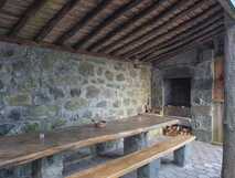 Casas do Capelo auf Faial, rustikaler überdachter Außenbereich mit Holztisch, Bänken und gemauertem Grillplatz vor einer Steinwand.