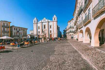 Der Hauptplatz der Stadt Evora, Portugal, umgeben von einer schicken Häuserreihe und vielen Freisitzen direkt unter blauem Himmel.