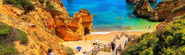 Eine kleine Bucht mit türkisblauem Wasser, gelben Sandstränden und gelb-braunen Felsformationen, ein Bild eines Traumstrandes an der Süd-Küste in Portugal