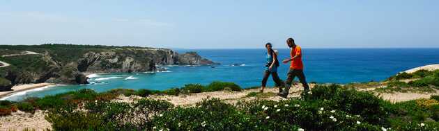 2 Personen wandern entlang der Küste Portugals am Meer mit atemberaubenden Blick über die Bucht.