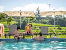 Familie mit Kindern am Pool des Palacio Santa Catarina Hotels auf den Azoren mit Liegestühlen, Sonnenschirmen und grüner Landschaft