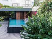Kleiner Außenpool mit Holzdeck und Liegestühlen, umgeben von dichter Vegetation.