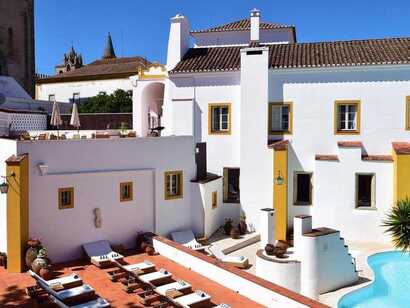 Blick in den Innenhof einer historischen und stilvollen Unterkunft mit weiß getünchten Wänden, Pool und Liegen zum Entspannen