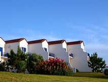 Weiße Reihenhäuser mit blauen Balkonen und roten Dächern im Ocidental Hotel auf Faial, umgeben von Garten und Blumen