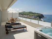 Private Terrasse der Sul Villas & Spa mit Whirlpool, Sonnenliegen und Meerblick auf die grüne Küstenlandschaft von São Miguel.