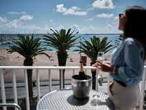 Frau mit Glas Sekt auf dem Balkon des Varandas do Atlântico Hotels mit Blick auf Palmen, Strand und den Atlantik.