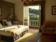 Helles Hotelzimmer mit großem Bett, Sofa und offenem Balkon mit Blick auf die umliegende Landschaft