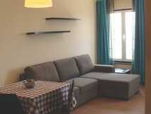 Apartaments Kosmos auf der Insel Faial, gemütliches Wohnzimmer mit grauem Ecksofa, blau kariertem Tischdeckenüberzogenen Esstisch und großen Fenstern mit blauen Vorhängen.