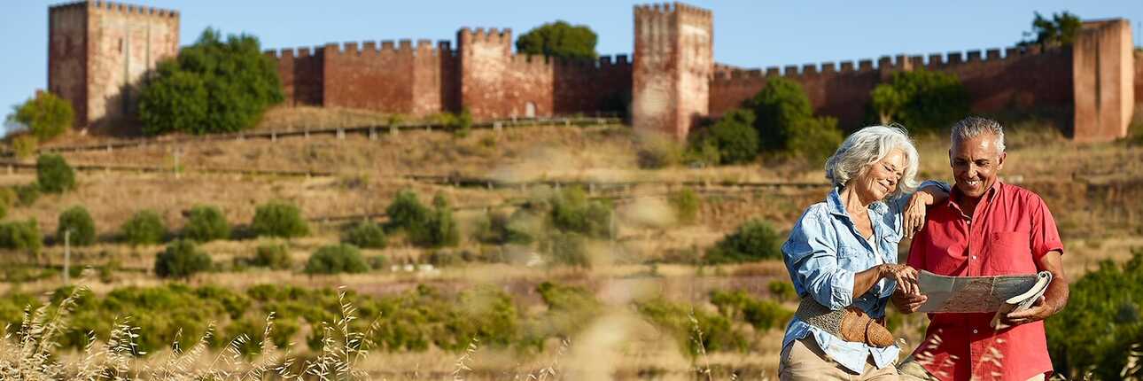 Älteres Paar studiert die Landkarte auf einem Feld vor einer Burg.