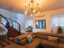 Gemütliches Wohnzimmer mit bequemer Couch, modernem Kronleuchter und eleganter Wendeltreppe.
