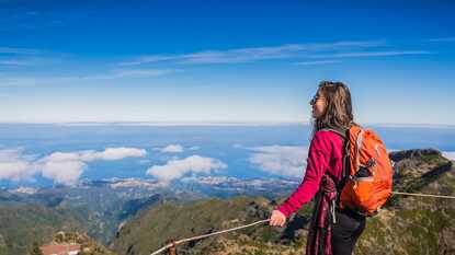 Eine Wanderin steht bei sonnigem Wetter auf dem Gipfel des Pico Ruivo und genießt die klare Aussicht auf die Berglandschaft Madeiras