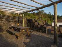 Casas do Capelo auf Faial, gemütliche Außensitzbereich mit Holztisch und Pergola, umgeben von Natur und traditionellem Steinmauerwerk.