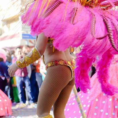 Karnevalstänzerin in pinkfarbenem Federkostüm tanzt durch die Straßen auf Kap Verde.