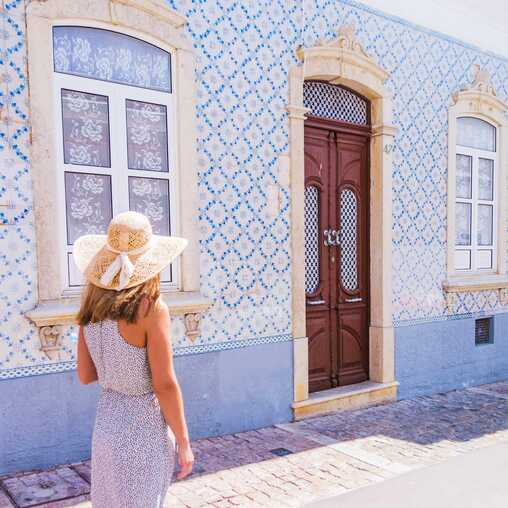 Ein Frau steht vor einer Hauswand mit Azulejos - kunstvolle Keramikfliesen in Portugal