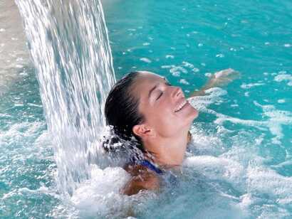 Eine bis zu den Schultern untergetauchte Frau erholt sich unter dem Wasserfall in einem Termalbad