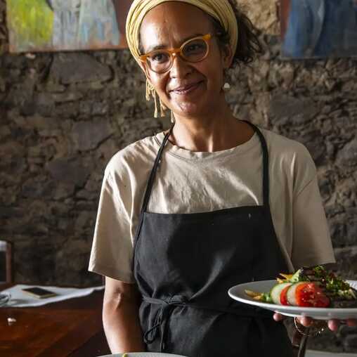 Lächelnde Kellnerin serviert ein traditionelles kapverdisches Gericht in einem lokalen Restaurant.