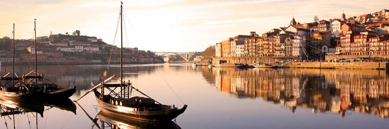 Porto – die kleine Schwester von Lissabon – im Sonnenuntergang mit Blick auf den Hafen und zwei Booten im Vordergrund.