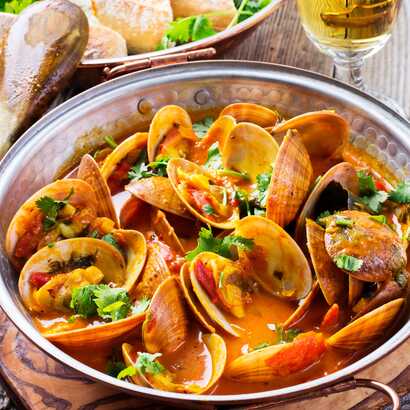 Typisch portugiesisches Muschelgericht mit Koriander in Weißweinsauce, serviert in einer Kupferpfanne.