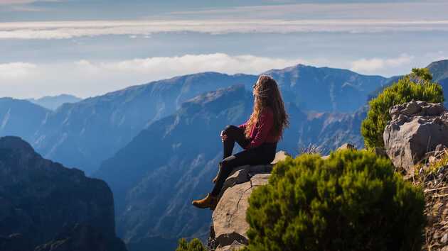 Eine Wanderin steht bei gutem Wetter auf dem Gipfel des Pico Ruivo und blickt über die weite Berglandschaft