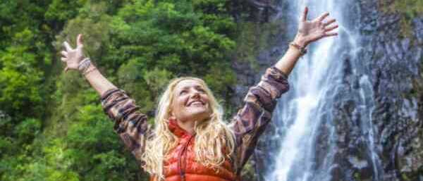 Frau mit erhobenen Armen vor einem Wasserfall auf Madeira