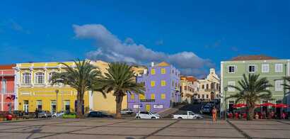 Bunte Kolonialgebäude am Platz in Mindelo auf São Vicente mit Palmen und Straßencafé.